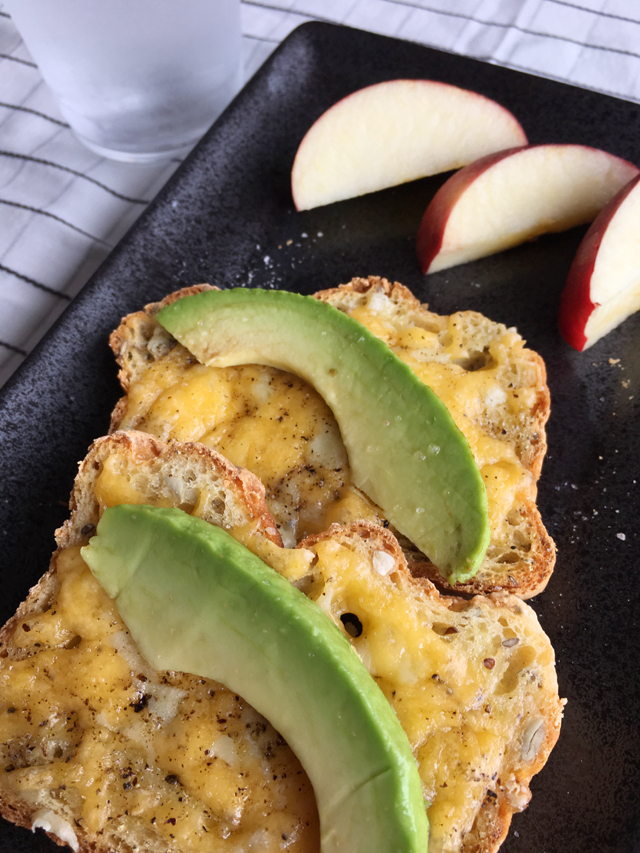 Slices of avocado on Broiled Cheese Toasts on a black plate with apple slices