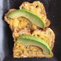 Two broiled cheese toasts with avocado slices on a plate