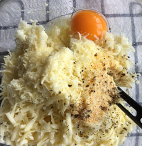 A bowl of cooked grated, cauliflower, egg, cheese, and seasonings