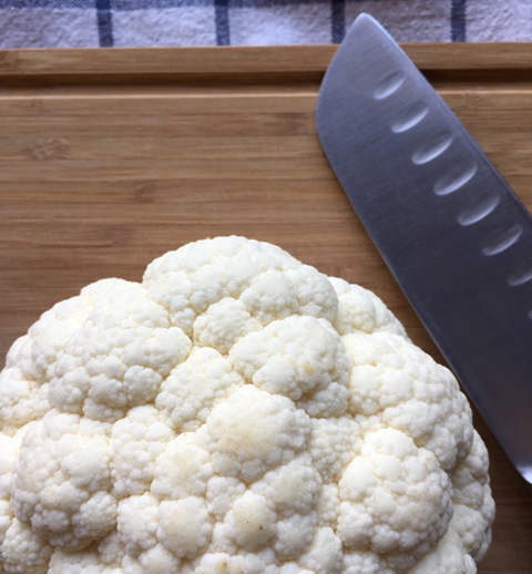 A head of cauliflower and knife on a cutting board in preparation for cauliflower pizza crust