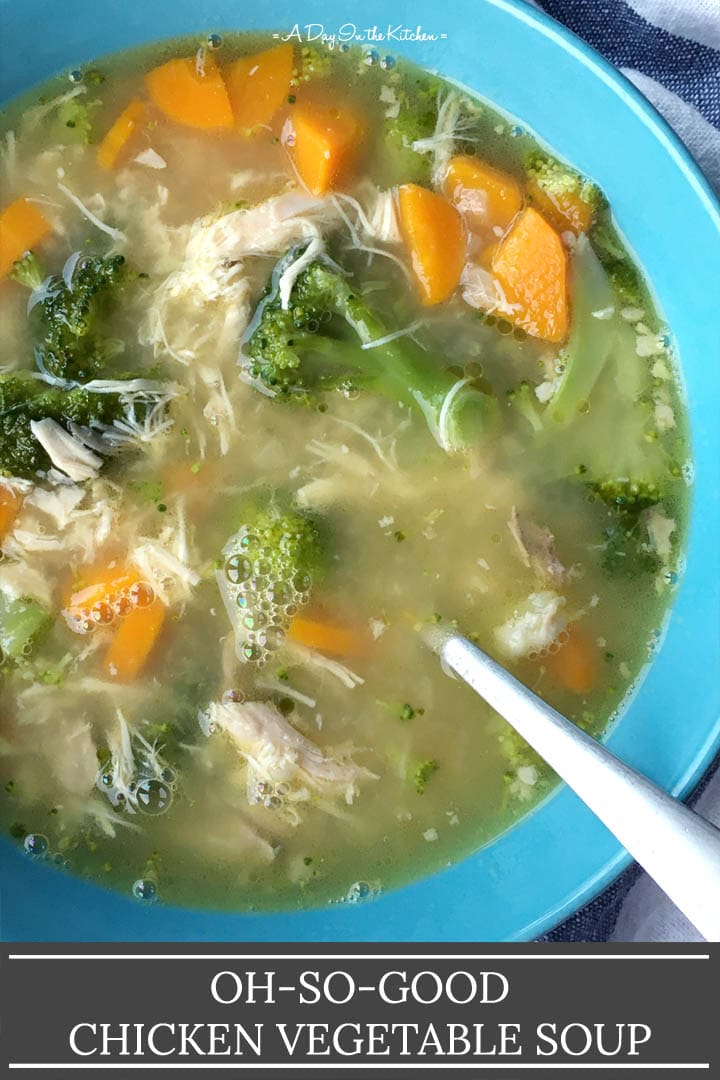 A spoon in a round blue bowl containing chicken vegetable soup with carrots, broccoli, and shredded chicken