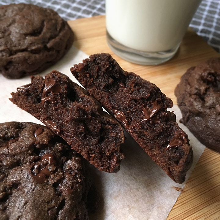 Close-up of a chocolate cookie split in half next to a glass of milk