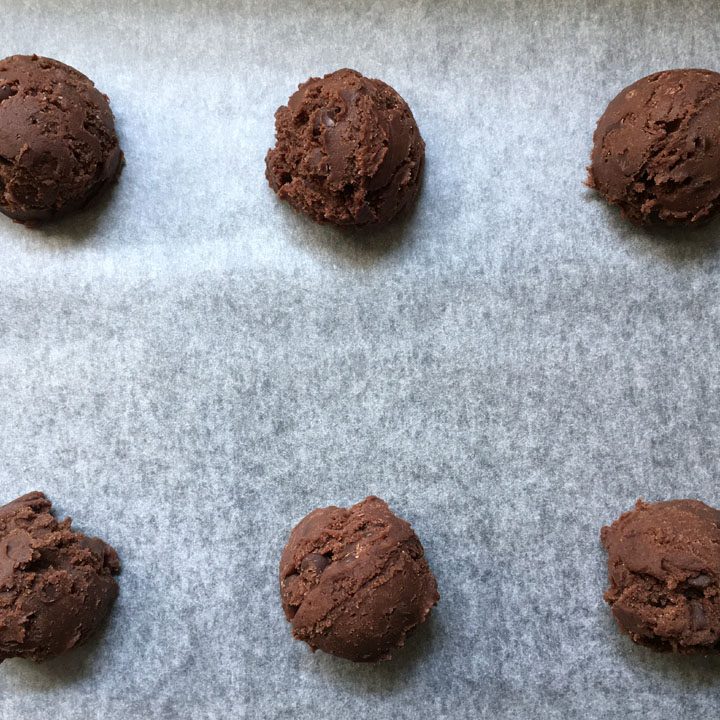 Six balls of brown cookie dough balls on a baking sheet
