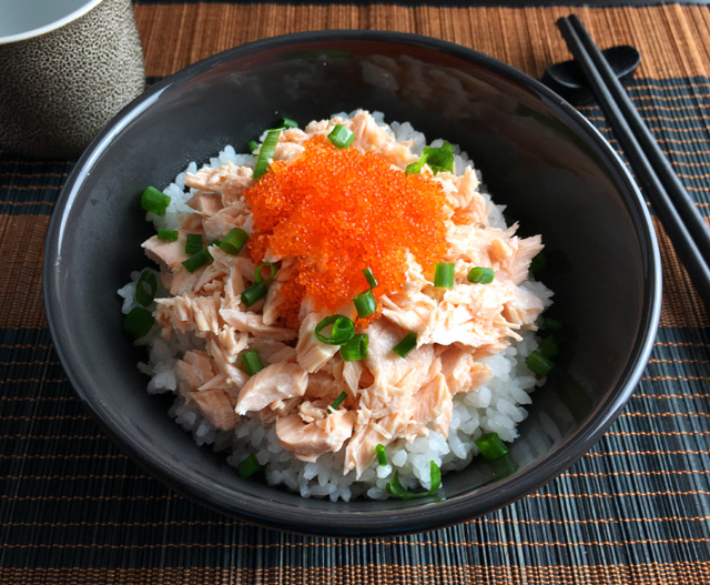 A Poached Salmon Tobiko Bowl on a brown and black bamboo platemat with chopsticks and a teacup