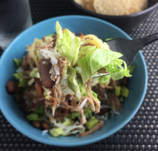A forkful of lettuce, pulled pork, rice, and beans from Carnitas Fiesta Bowls