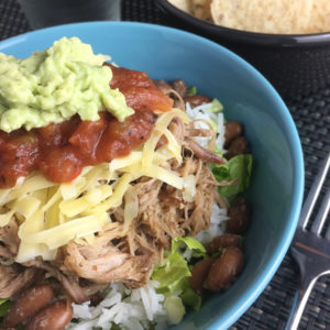 A bowl with rice, beans, pulled pork, lettuce, cheese, salsa, and guacamole