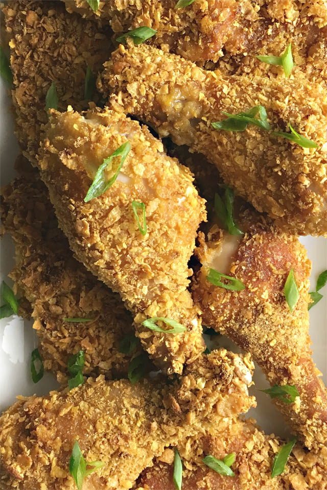 A white platter containing several pieces of cornflakes chicken sprinkled with chopped green onions