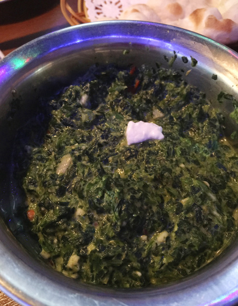 A metal bowl filled with palaak paneer at Hungry Eye Restaurant