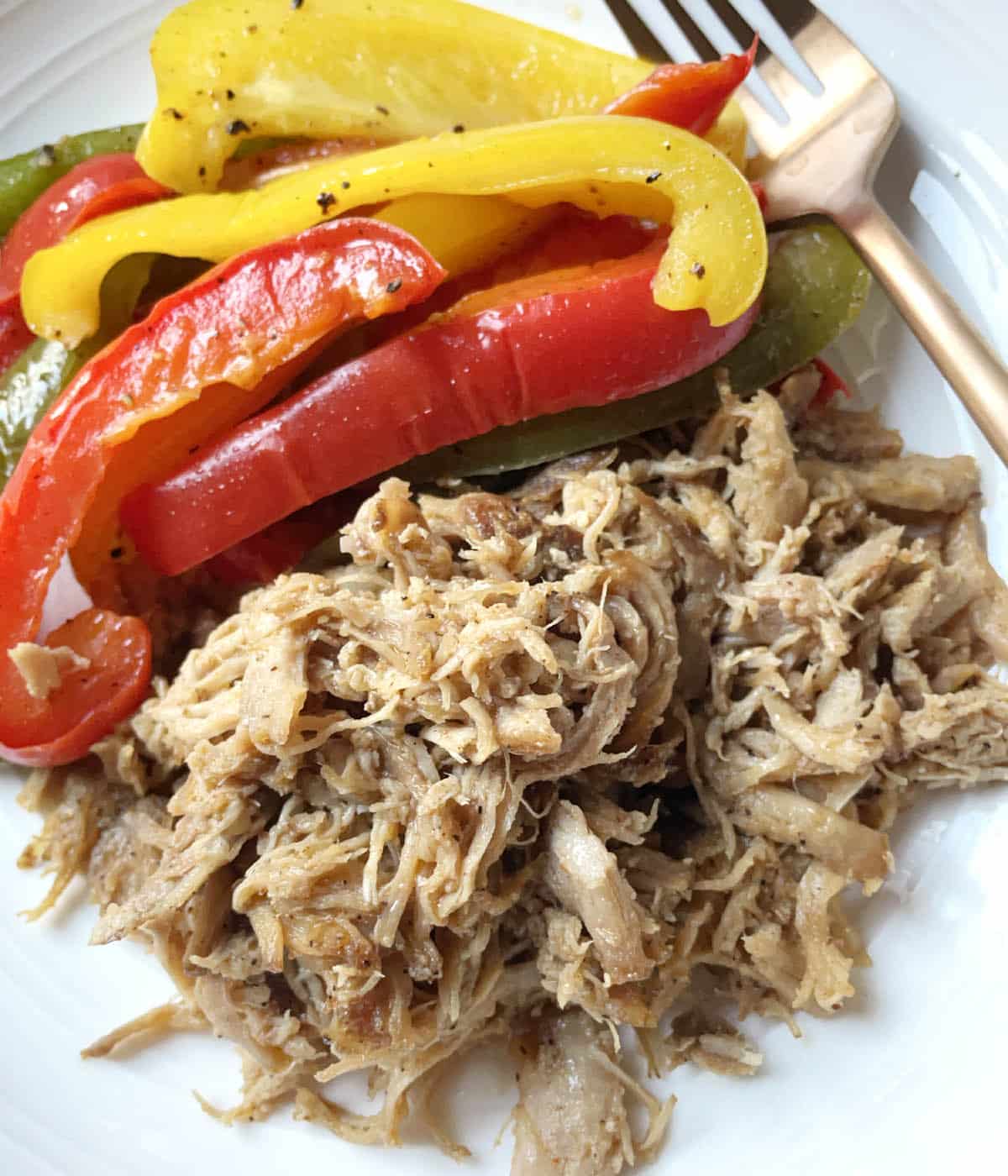 A white dish containing a fork, pulled pork, and slices of red, green, and yello bell peppers.