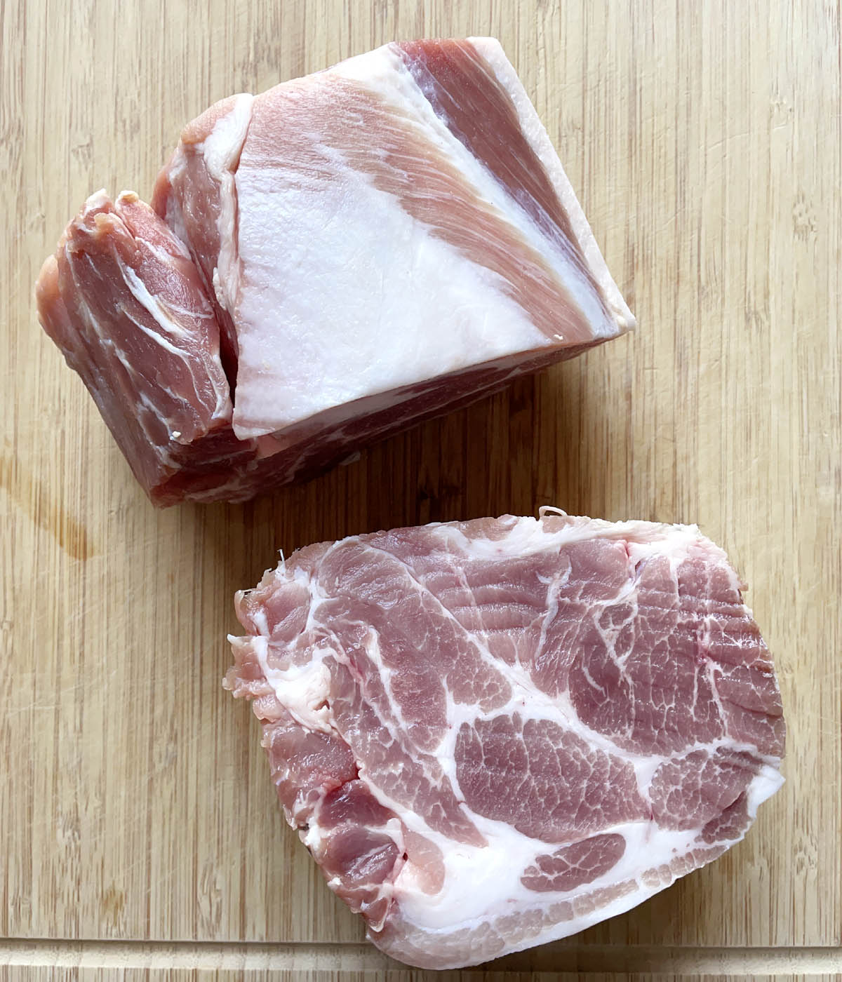 A raw chunk of pork roast, cut into two chunks on a wooden cutting board.
