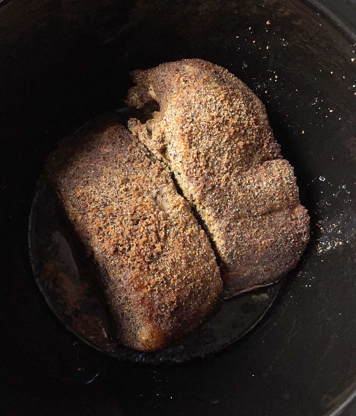 Two cooked chunks of seasoned pork in a black pot.