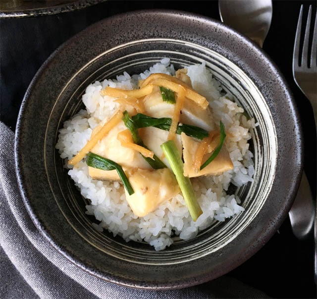 A dark round bowl containing white rice and poached black cod with ginger and green onions