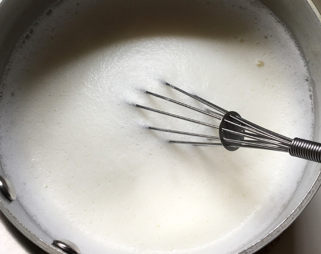 A metal whisk in frothy milk in a pot for English tea latte
