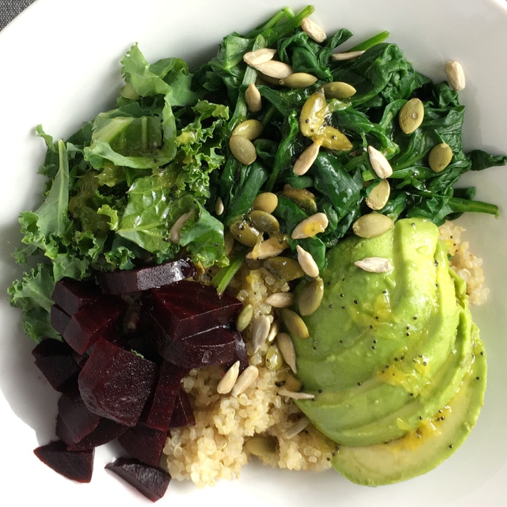 A white bowl containing beets, quinoa, avocado, spinach, kale, and seeds