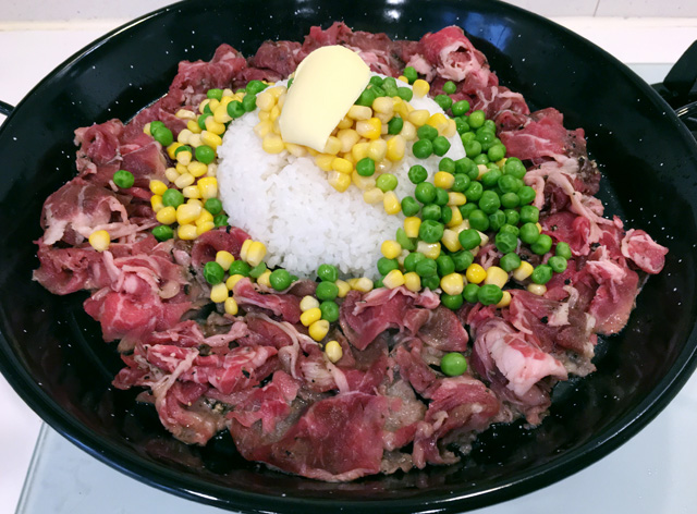 A black pan of raw beef, white rice, corn, peas, and butter for Pepper Beef Rice Skillet
