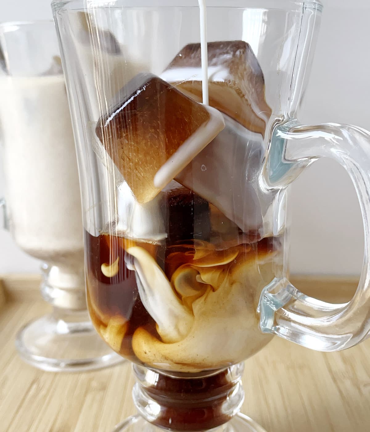 Milk being poured into a glass mug containing coffee ice cubes.