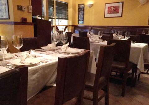 Tables with place settings and wine glasses and chairs in the dining room at La Pampa