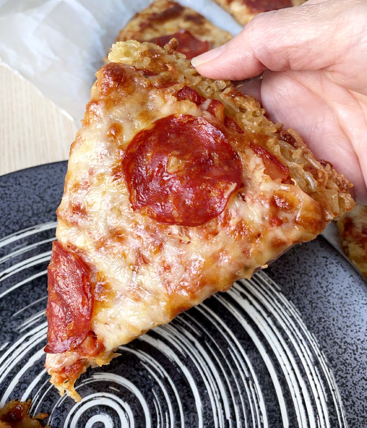 A hand holding a slice of rice crust pizza.