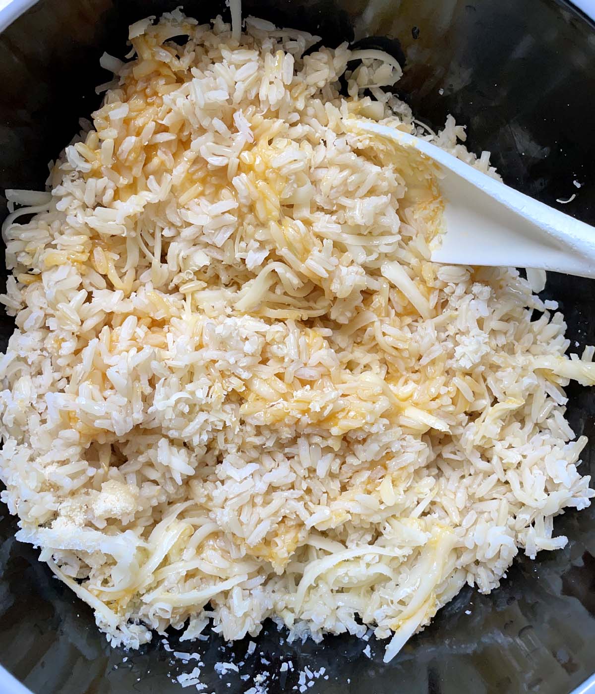 A white spoon mixing together cooked rice, egg and cheese in a bowl.