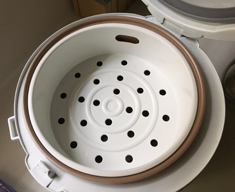 A white steaming tray in a rice cooker to make Eggs in a Rice Cooker