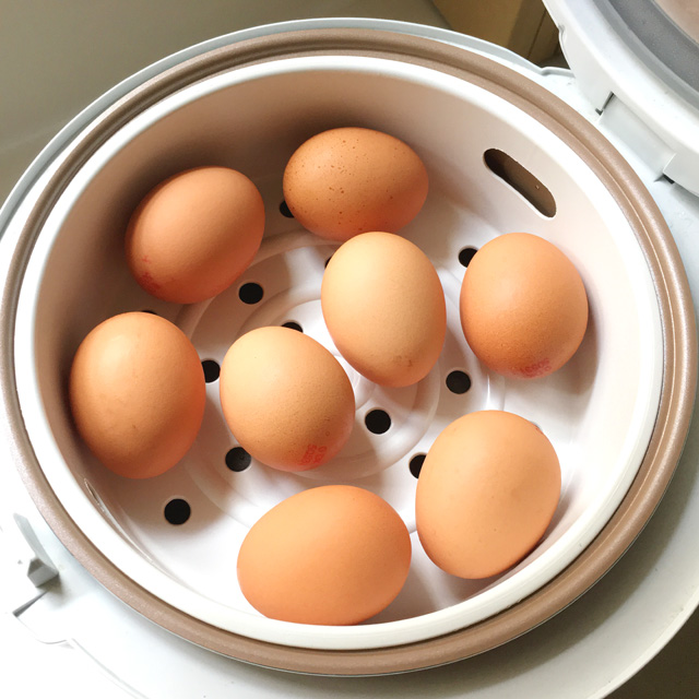 Eight brown eggs in a white steamer basket in a rice cooker