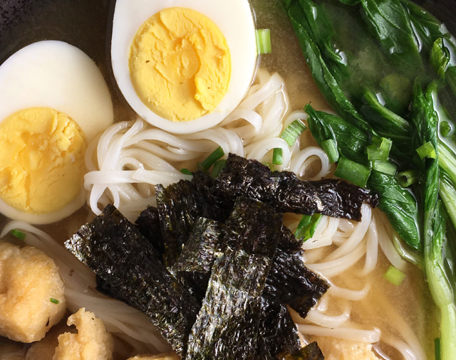 Miso Noodle Soup containing rice noodles, hard cooked egg, leafy green vegetables, tofu puffs, and roasted sewaeed