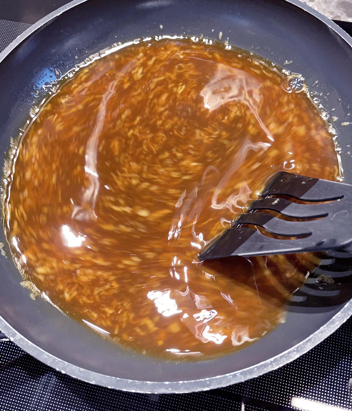 A black spatula stirring brown sauce in a pan.