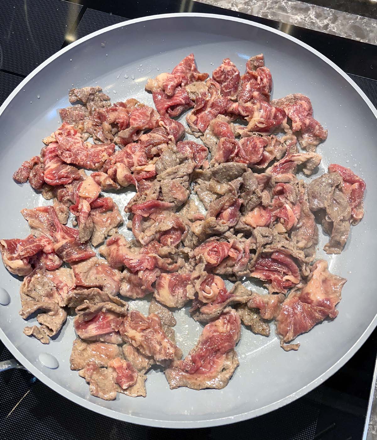 Raw slices of beef being cooked in a round grey pan.