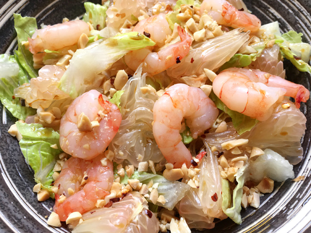 A stone bowl containing lettuce, pomelo wedges, shrimp, and chopped peanuts