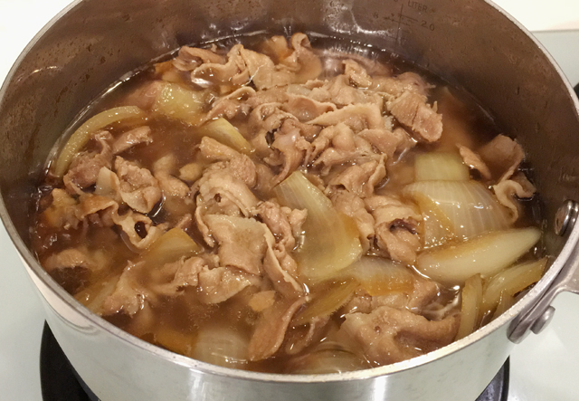 A pot containing pork and onions in a brown liquid for butadon pork bowls