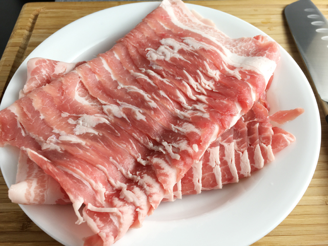 A white round plate containing raw pork belly slices