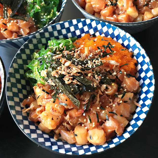 A blue and white bowl containing chopped salmon and shrimp, green seaweed salad, and orange fish eggs
