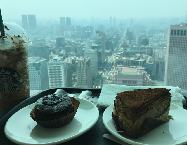 A closeup of Starbucks drinks and food with a view of Taipei in the background