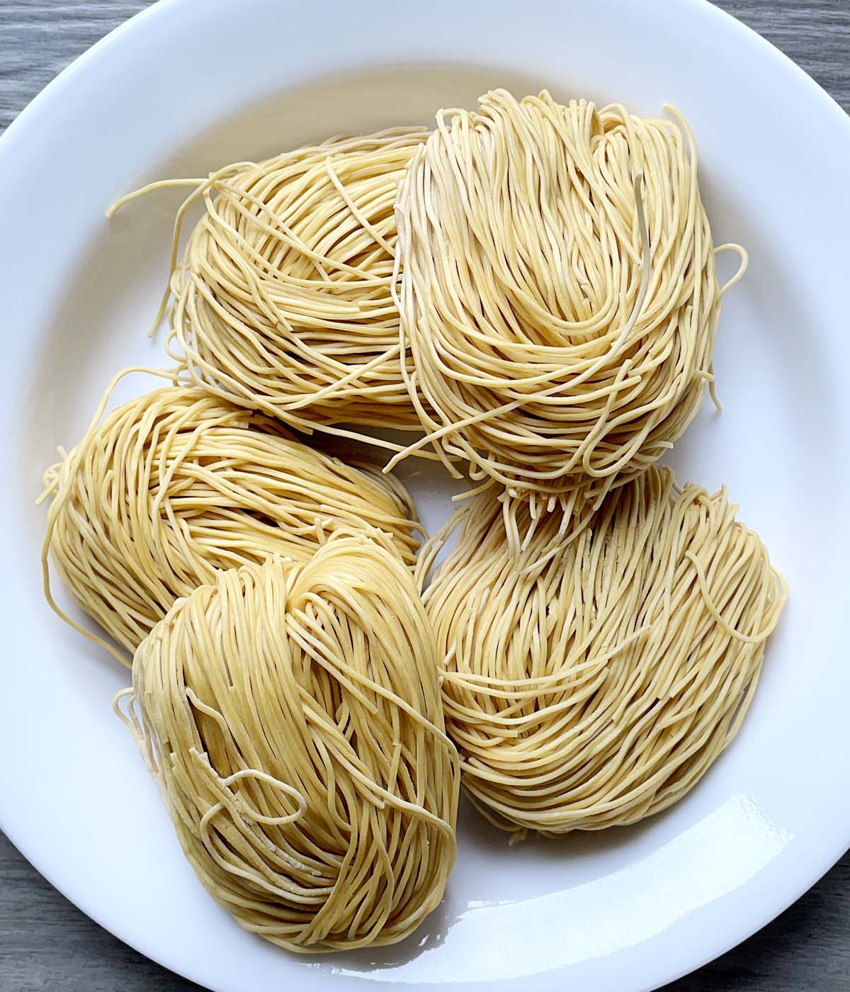 A white plate containing five bundles of dried yellow noodles.