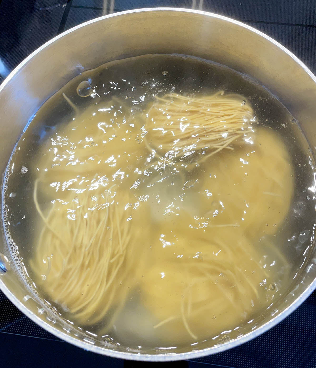Five bundles of dried noodles in a pot of boiling water.