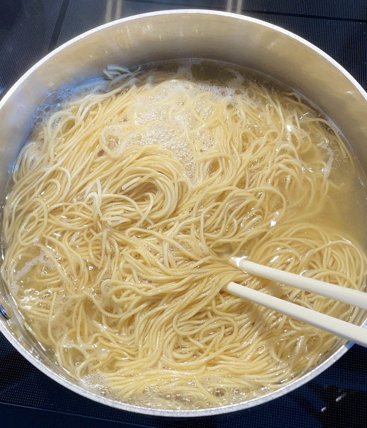 Chopsticks stirring loosened noodles in a pot of boiling water.