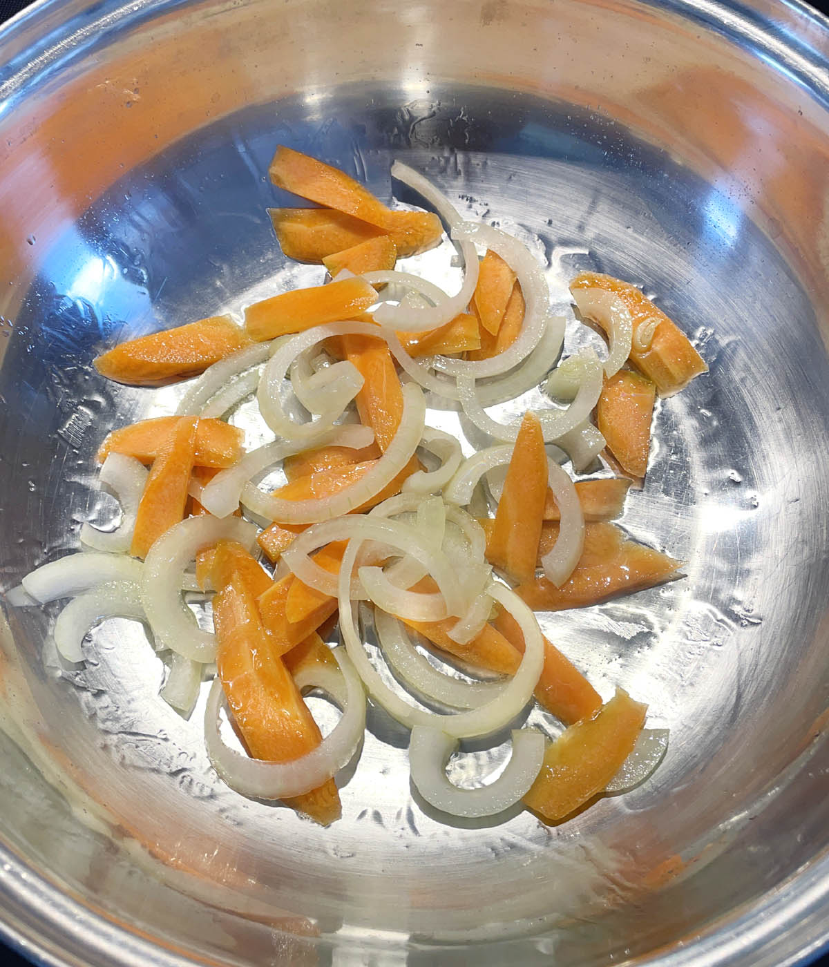 Sliced carrots and onions in a metal wok.