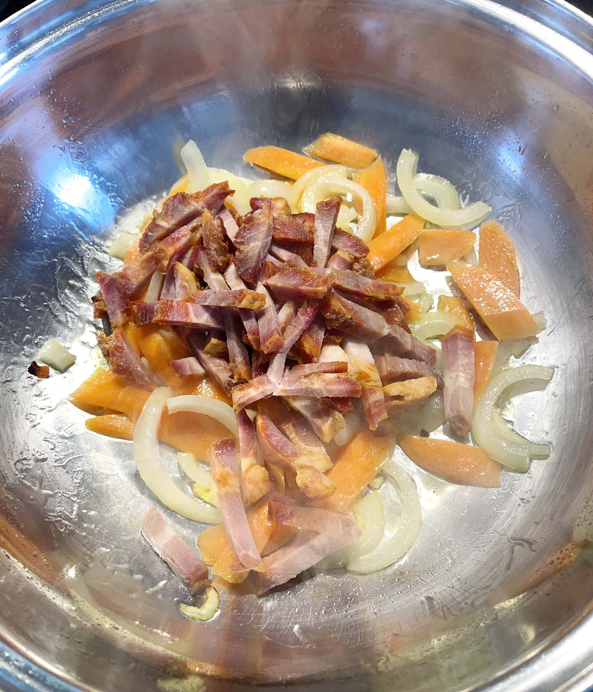 Chunks of barbecue pork, sliced onions and carrots cooking in a metal wok.