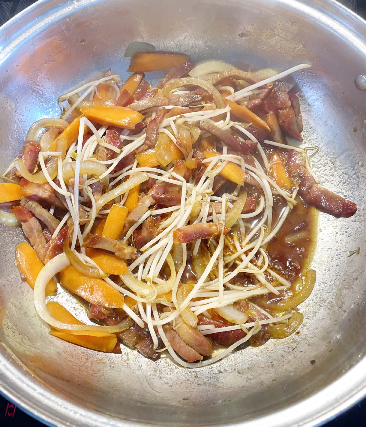 A round metal wok containing carrots, onions, bean sprouts, and meat in a brown sauce.