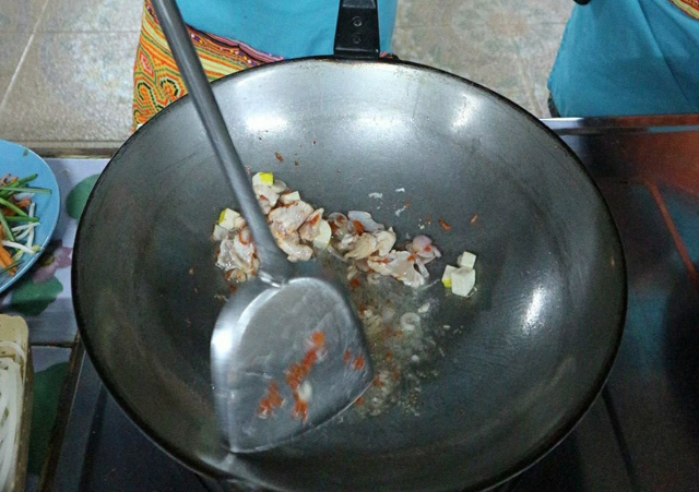 Chicken, onions, tofu and chili peppers being cooked in a large silver wok with a stainless steel spatula in Chiang Mai