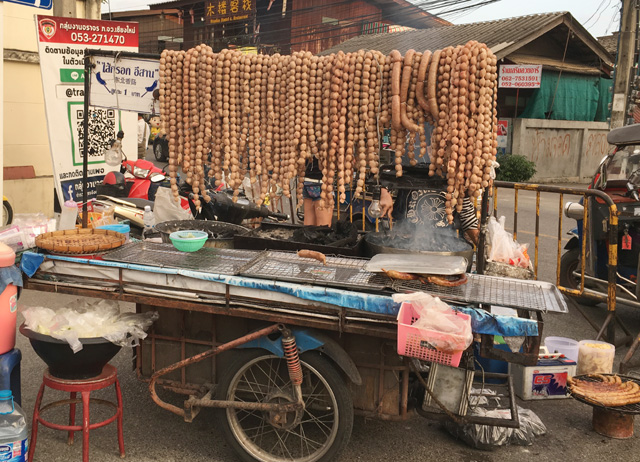 A cart on wheels, with a cooking grill and an assortment of meatballs and weiners at the Saturday Night Market in Chiang Mai