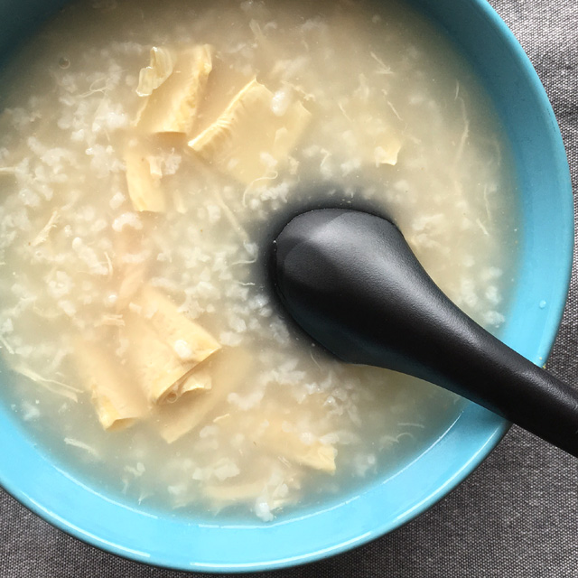 A black spoon in a blue bowl containing Chinese rice porridge congee