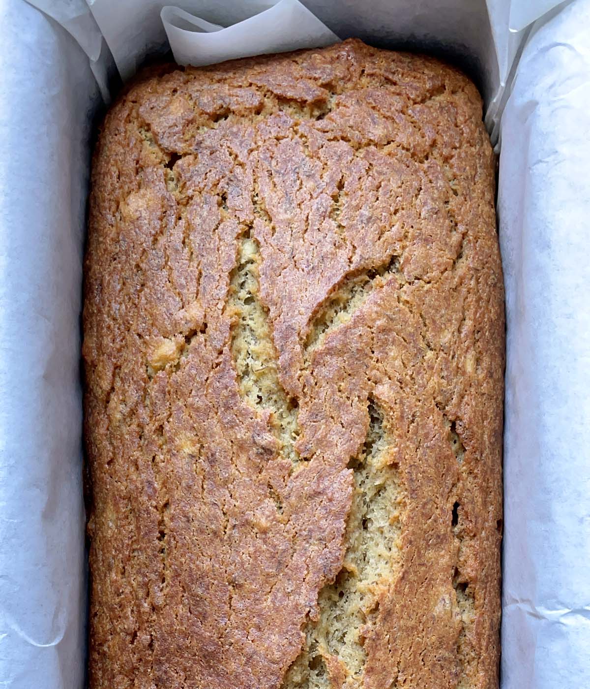A brown baked banana bread in a paper lined pan.