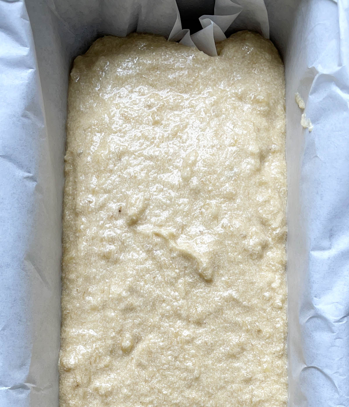 Raw bread batter in a paper lined pan.
