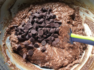 Brown chocolate chips being mixed into flourless chocolate chocolate chip muffin batter in a round metal bowl