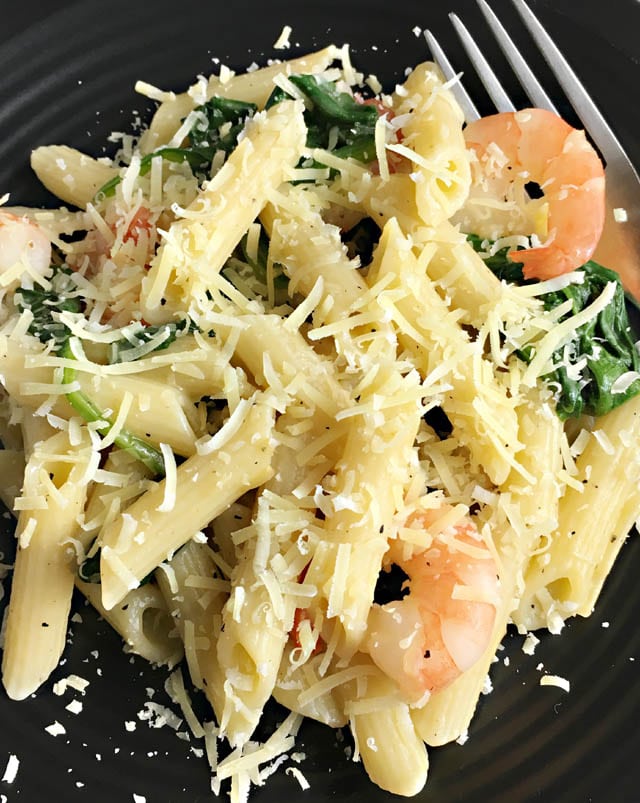 A black plate containing pasta, shrimp and spinach covered in Parmesan cheese