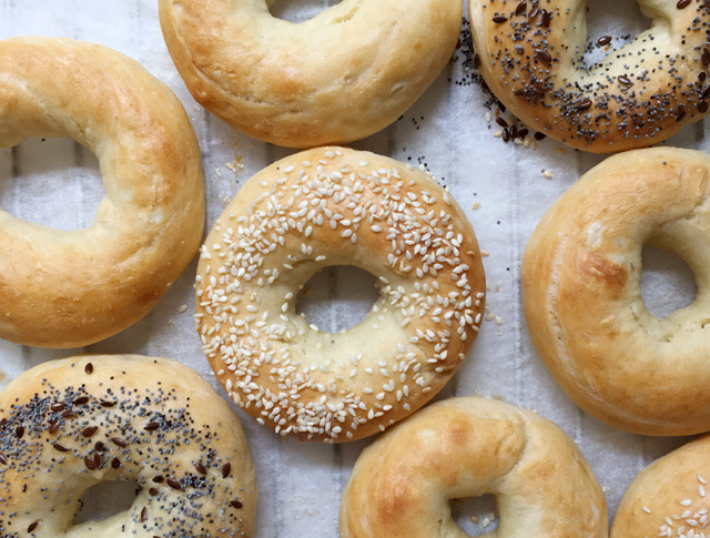 Plain, sesame, and poppyseed topped homemade bagels on white parchment paper