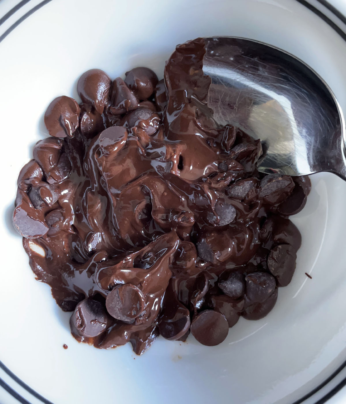 A spoon in a white bowl containing partially melted chocolate chips.