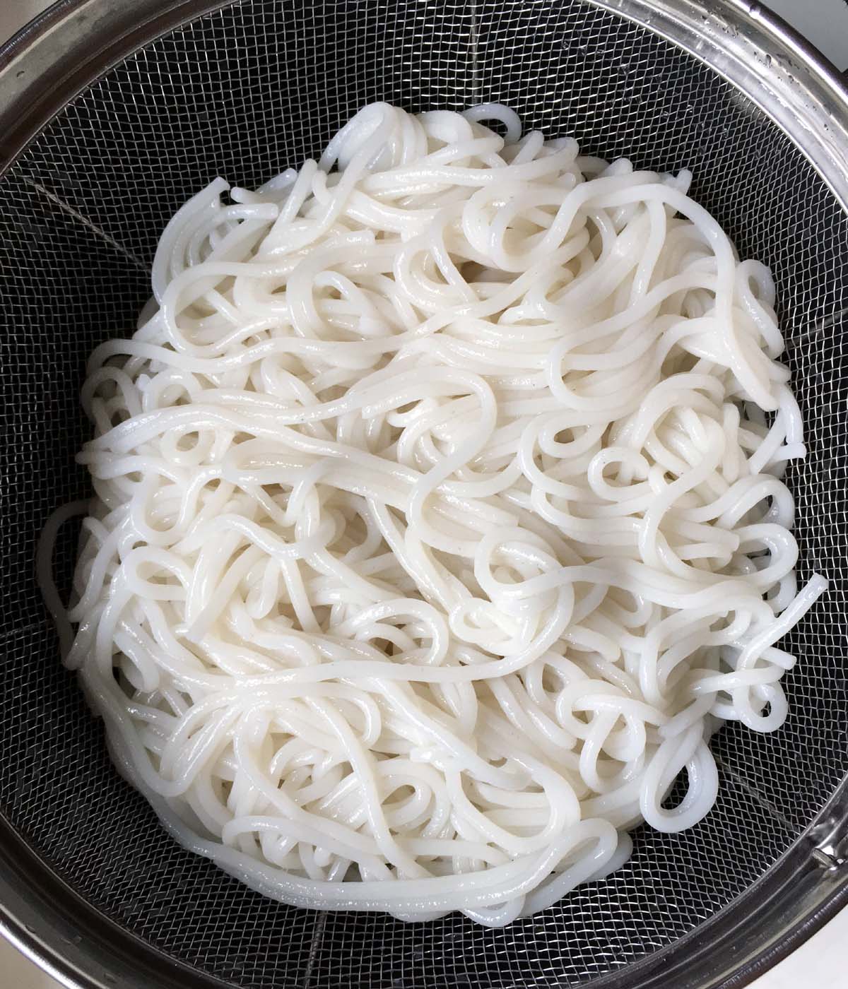 A colander containing cooked white noodles.