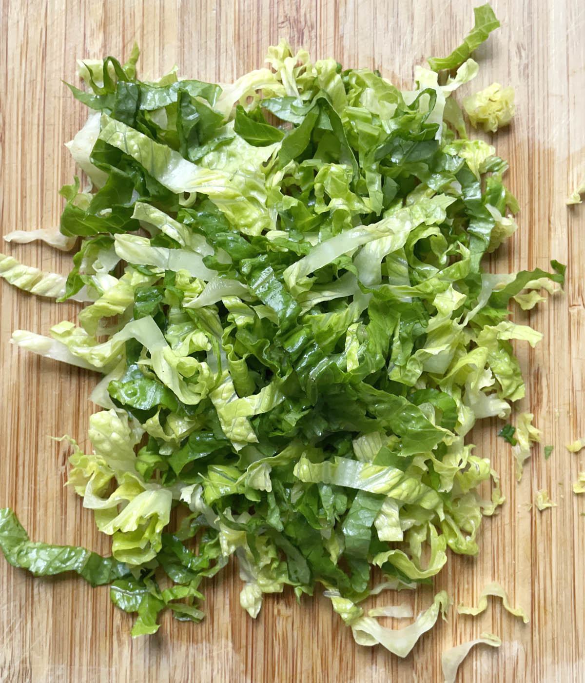 Finely chopped lettuce on a wooden cutting board.